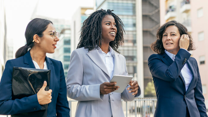 Three women dressed in business attire walking in a city.