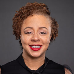 Headshot photo of Denine Das who is facing the viewer and smiling. She is wearing red lipstick and a black short sleeve blouse