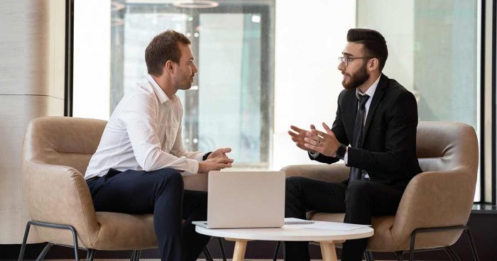 Two men in business attire having a meeting next to a laptop