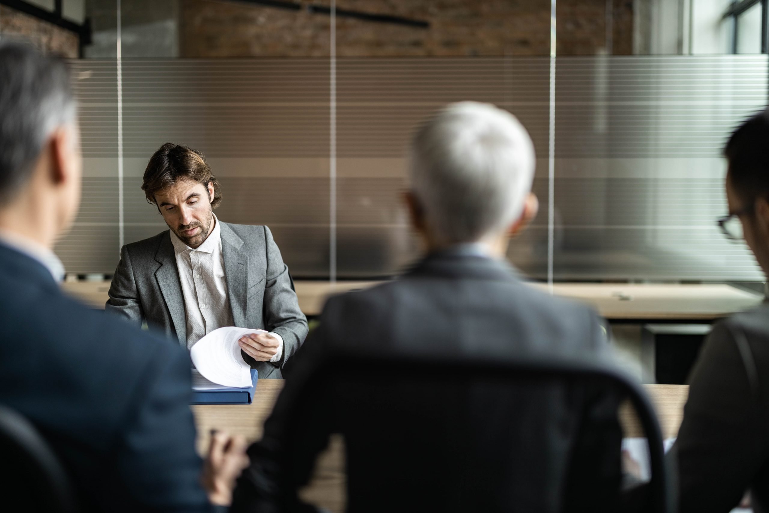 man sitting in distance across from other men at a board room table