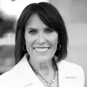 headshot of Jennifer McCollum who has a short bob haircut with a sideswept bangs and is wearing a white collared shirt. She is smiling at the camera. The photo is in greyscale.