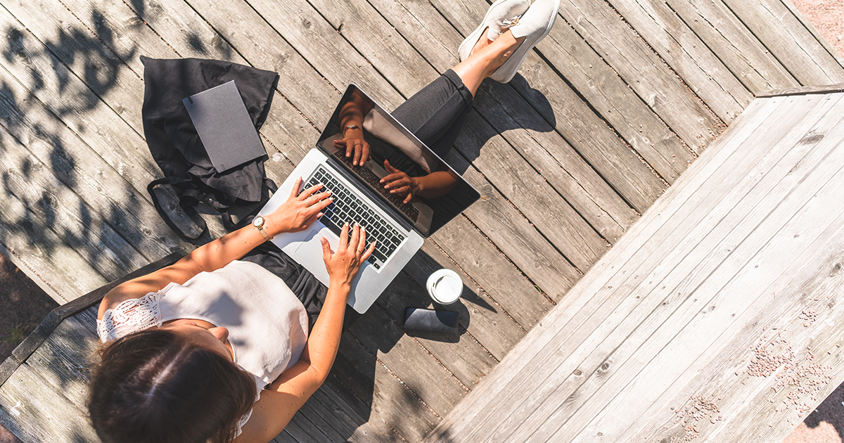 A lady works on her laptop while sitting on a deck.