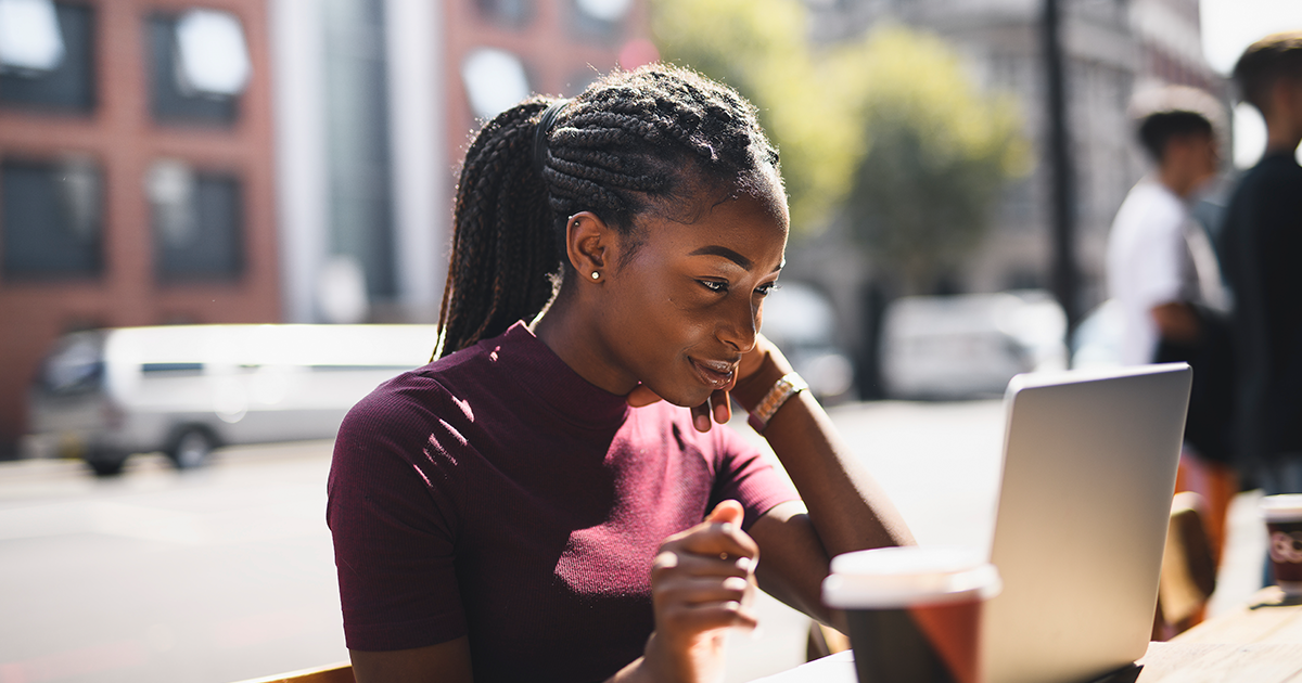 A young businesswoman working outdoors at a bistro on her laptop.