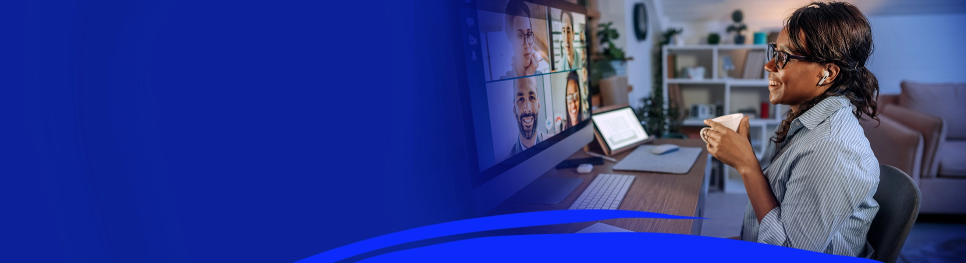header banner for inclusive hybrid workplaces, showing a woman sitting at her desk holding a cup, while on a conference call with multiple colleagues who can be seen on the computer screen.