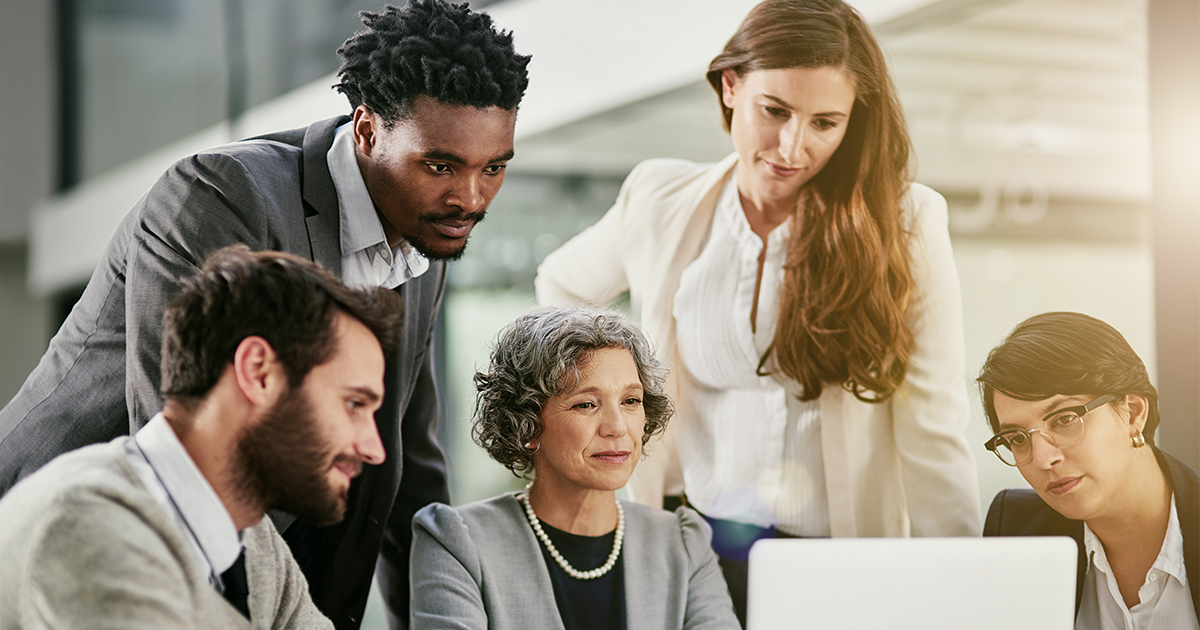 woman leader sitting at computer, surrounded by group of men and women looking at the computer monitor